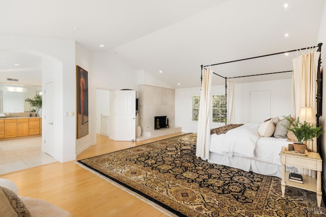 bedroom with light hardwood / wood-style floors, ensuite bathroom, and lofted ceiling