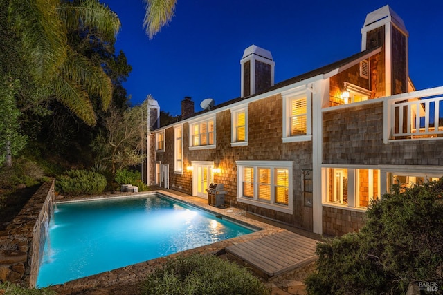 back house at night featuring pool water feature