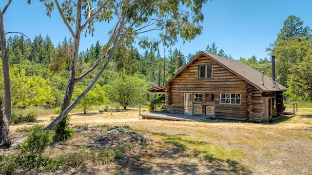 back of property with log siding, a porch, and a view of trees