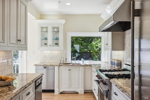 kitchen with wall chimney range hood, light hardwood / wood-style floors, stainless steel appliances, tasteful backsplash, and sink