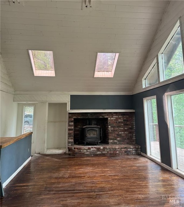 unfurnished living room with a skylight, plenty of natural light, high vaulted ceiling, and a wood stove