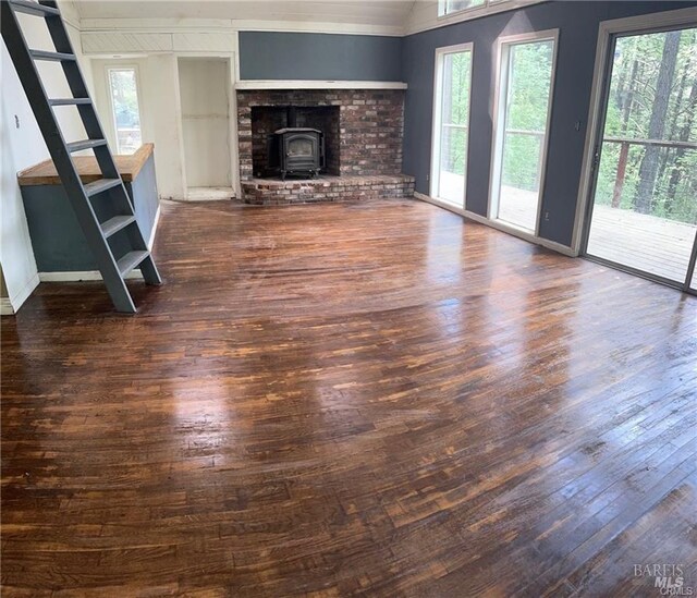 unfurnished living room with a healthy amount of sunlight, a wood stove, ornamental molding, and dark wood-type flooring