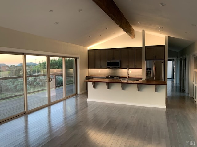 kitchen featuring stainless steel appliances, a kitchen breakfast bar, backsplash, hardwood / wood-style flooring, and vaulted ceiling with beams