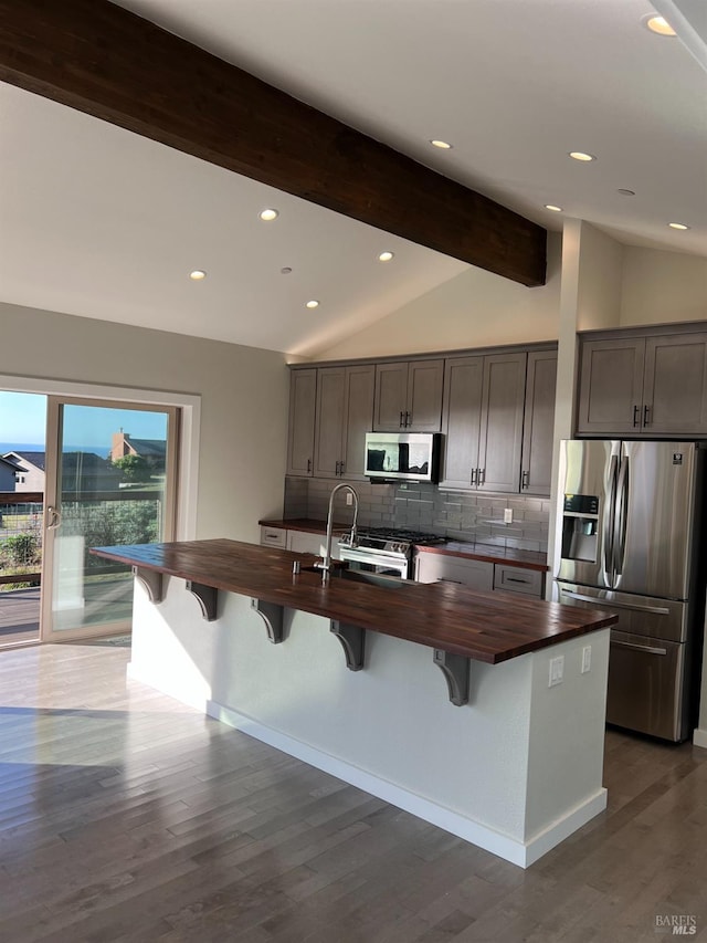 kitchen featuring appliances with stainless steel finishes, a kitchen island with sink, lofted ceiling with beams, and dark hardwood / wood-style flooring