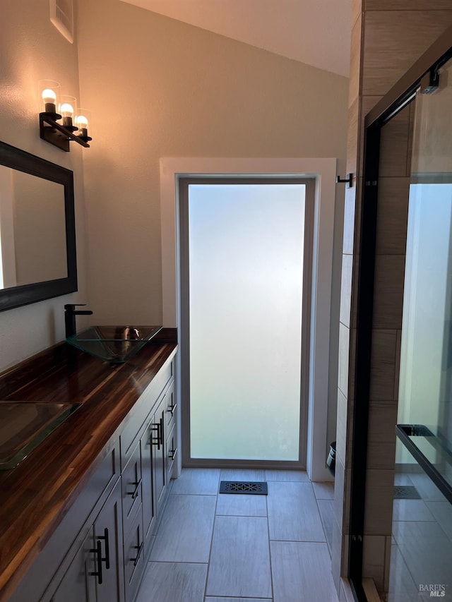 bathroom with tile floors, a shower with door, double sink vanity, and vaulted ceiling