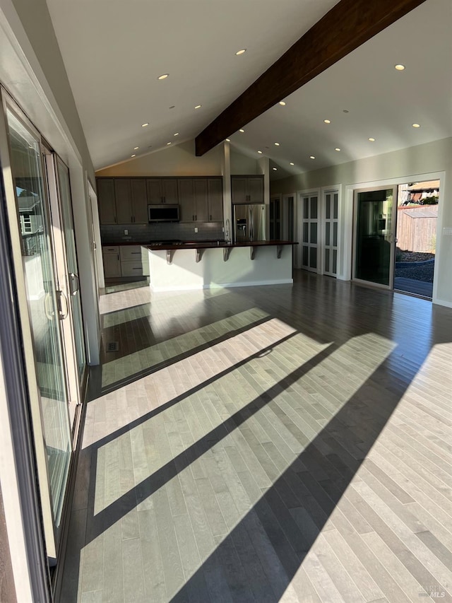 kitchen with a kitchen island with sink, a kitchen bar, wood-type flooring, appliances with stainless steel finishes, and lofted ceiling with beams