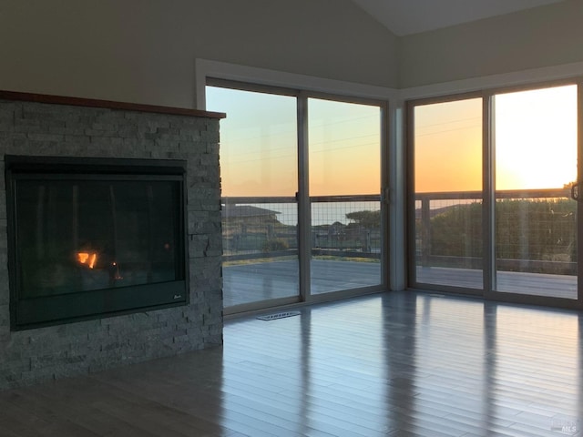 unfurnished living room with wood-type flooring, a stone fireplace, and vaulted ceiling