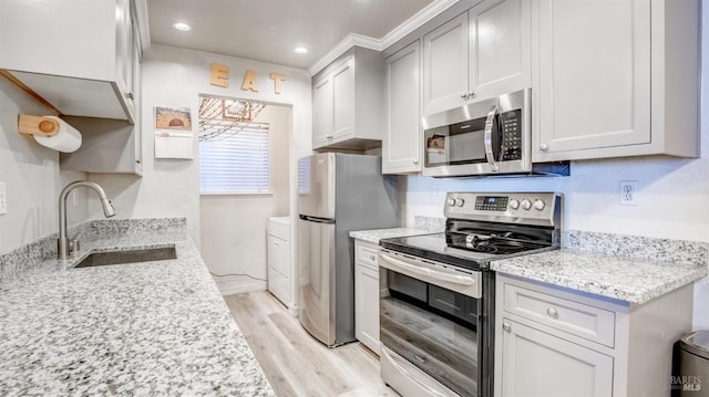 kitchen with light stone counters, light hardwood / wood-style floors, stainless steel appliances, ornamental molding, and sink