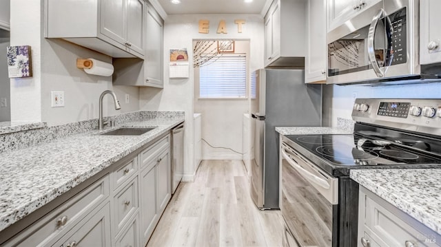 kitchen featuring appliances with stainless steel finishes, sink, light stone countertops, and light hardwood / wood-style flooring