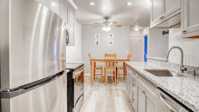 kitchen with light stone counters, light hardwood / wood-style floors, ceiling fan, appliances with stainless steel finishes, and sink