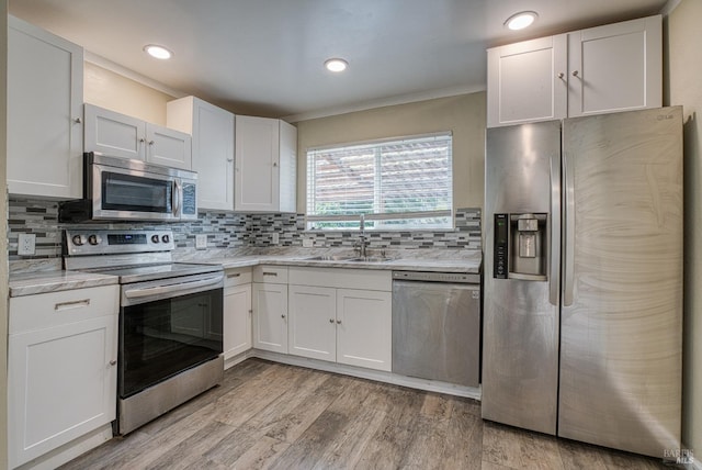 kitchen with backsplash, appliances with stainless steel finishes, sink, light wood-type flooring, and white cabinets