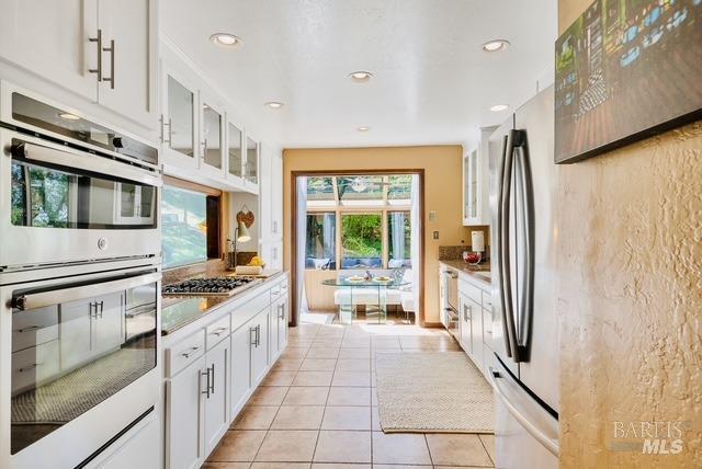 kitchen with glass insert cabinets, white cabinets, light tile patterned floors, and appliances with stainless steel finishes