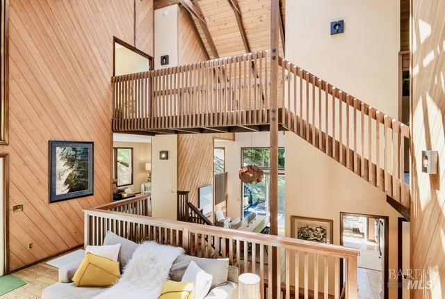 living room with a high ceiling, wood walls, wood finished floors, wood ceiling, and beam ceiling