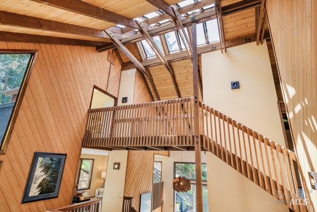 interior space featuring wood walls, a skylight, a towering ceiling, and beam ceiling