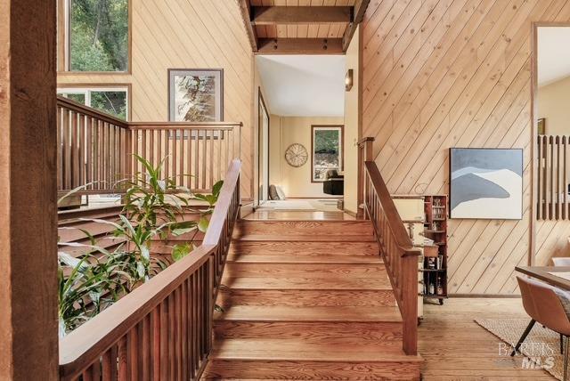 staircase with high vaulted ceiling, beam ceiling, wooden walls, and wood finished floors