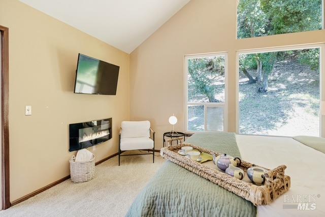 carpeted bedroom featuring high vaulted ceiling, a glass covered fireplace, and baseboards