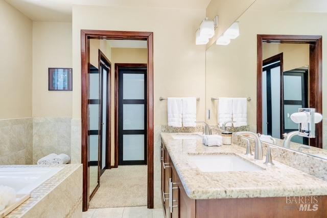 full bathroom with double vanity, tile patterned flooring, a sink, and a bath