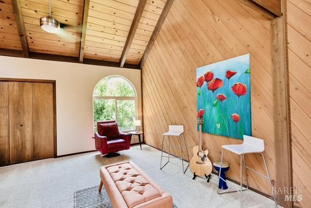 unfurnished room with vaulted ceiling with beams, wooden ceiling, carpet flooring, and wooden walls