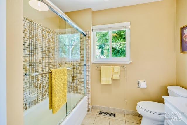 bathroom with visible vents, bath / shower combo with glass door, toilet, tile patterned flooring, and vanity