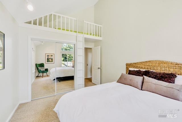 bedroom featuring baseboards, high vaulted ceiling, a closet, and light colored carpet