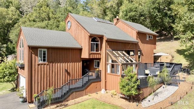 rear view of property with roof with shingles, a chimney, an attached garage, and driveway