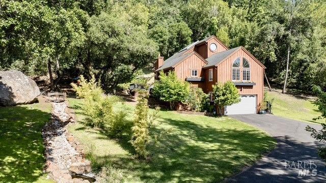 view of front of property with a front yard, a forest view, driveway, and an attached garage