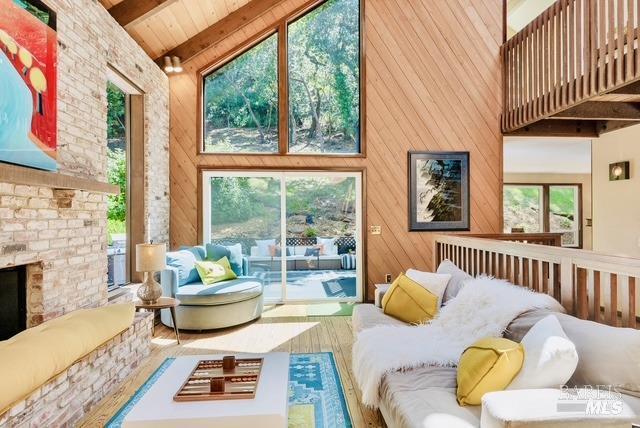 living room featuring high vaulted ceiling, beam ceiling, wooden walls, wood finished floors, and a brick fireplace
