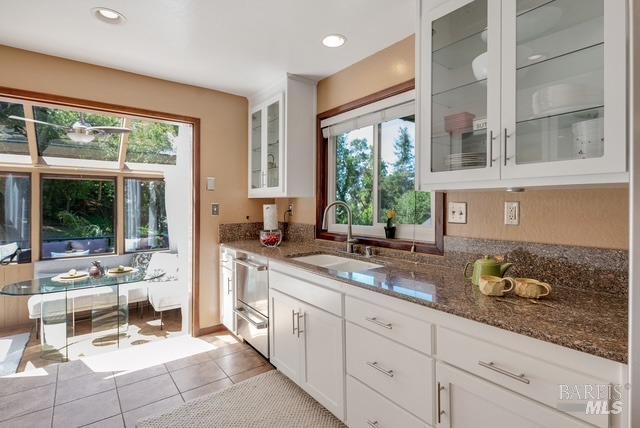 kitchen with a healthy amount of sunlight, light tile patterned floors, dark stone countertops, and a sink