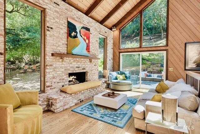 living room with wooden ceiling, high vaulted ceiling, beam ceiling, a brick fireplace, and wood finished floors