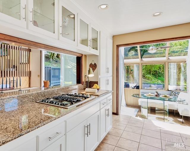kitchen with light stone countertops, plenty of natural light, stainless steel gas cooktop, and glass insert cabinets