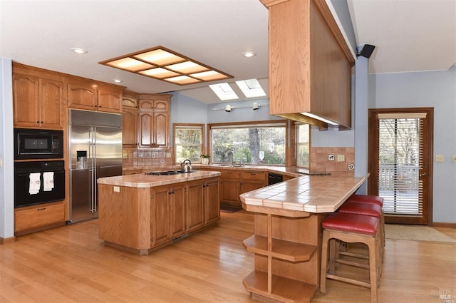 kitchen with tile countertops, light wood-type flooring, kitchen peninsula, and black appliances