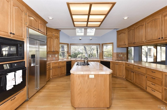 kitchen with light hardwood / wood-style floors, tile counters, a center island, tasteful backsplash, and black appliances