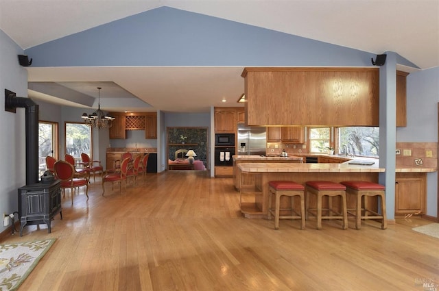 kitchen featuring kitchen peninsula, pendant lighting, light wood-type flooring, black appliances, and lofted ceiling