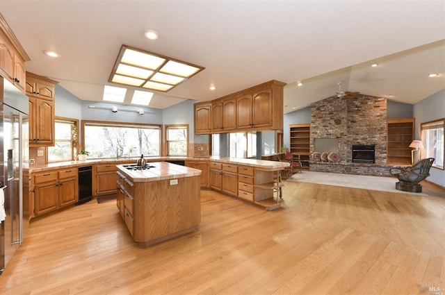 kitchen with kitchen peninsula, a kitchen island, vaulted ceiling, a fireplace, and light hardwood / wood-style floors