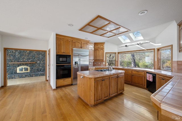 kitchen with black appliances, light hardwood / wood-style floors, a center island, and tile countertops