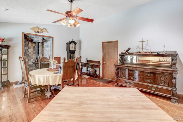 dining room featuring a wood stove, hardwood / wood-style floors, a textured ceiling, and ceiling fan