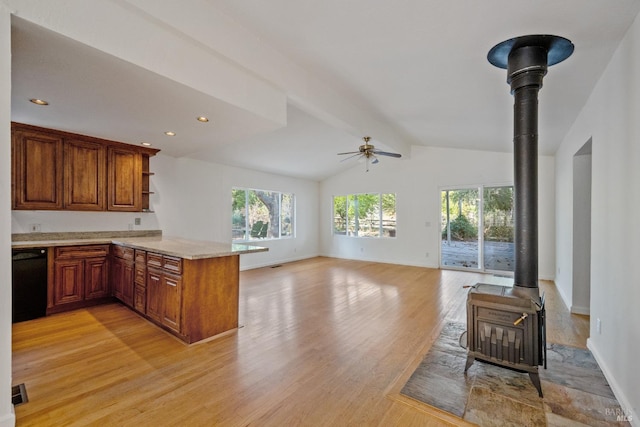 kitchen featuring ceiling fan, light hardwood / wood-style flooring, kitchen peninsula, vaulted ceiling, and a wood stove