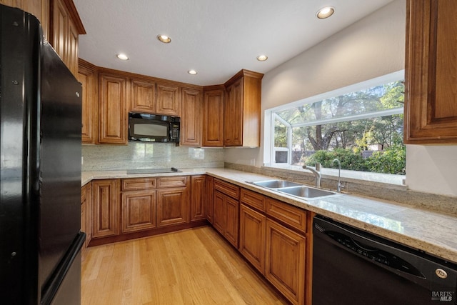 kitchen featuring light stone countertops, light wood-type flooring, black appliances, sink, and tasteful backsplash