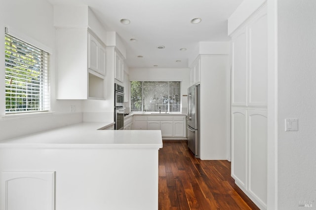 kitchen with dark wood-type flooring, stainless steel appliances, white cabinets, kitchen peninsula, and sink