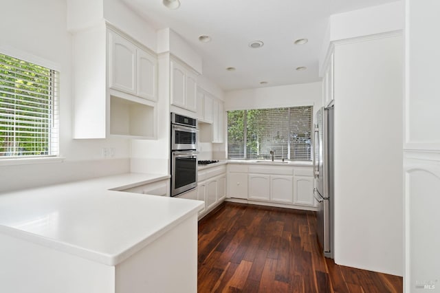 kitchen with dark wood-type flooring, appliances with stainless steel finishes, white cabinets, kitchen peninsula, and sink