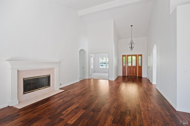 entrance foyer with dark wood-type flooring, a towering ceiling, beamed ceiling, and a tile fireplace