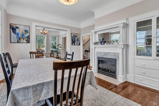 dining space featuring stairway, an inviting chandelier, a premium fireplace, wood finished floors, and baseboards