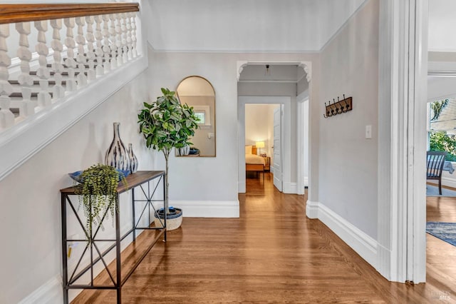 hallway with arched walkways, baseboards, and wood finished floors