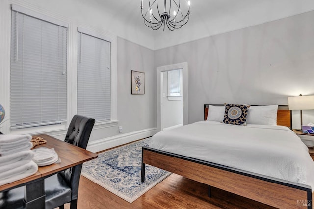 bedroom with a chandelier, wood finished floors, and baseboards