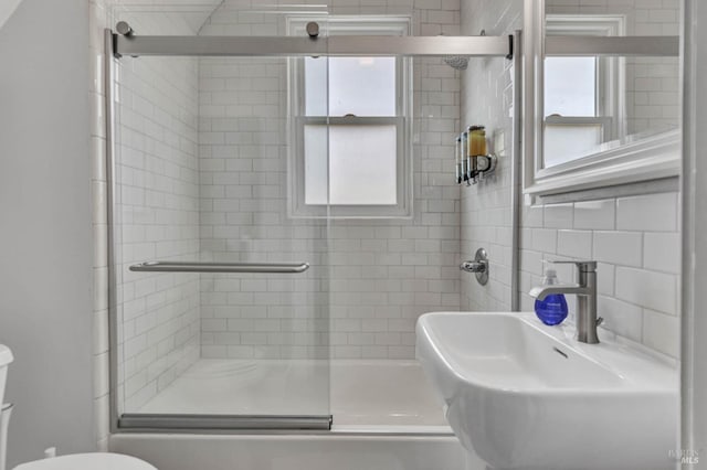 full bathroom with tile walls, a sink, toilet, and a shower stall