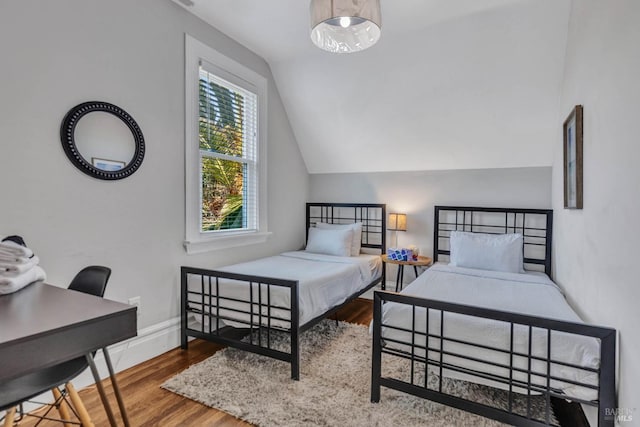 bedroom with vaulted ceiling, wood finished floors, and baseboards