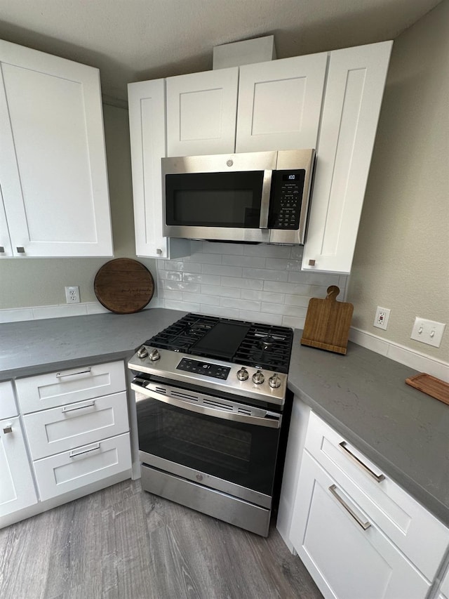 kitchen featuring stainless steel appliances, wood finished floors, white cabinets, and decorative backsplash