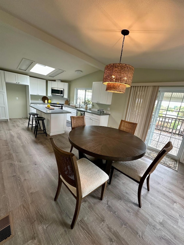 dining space with light wood finished floors, an inviting chandelier, vaulted ceiling, and visible vents
