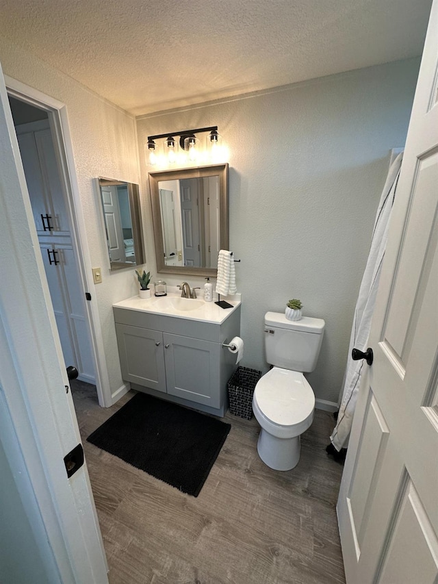 bathroom featuring a textured ceiling, toilet, vanity, wood finished floors, and a textured wall
