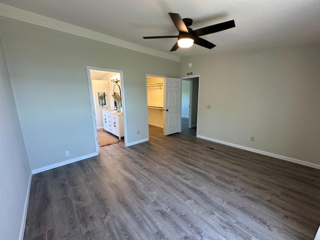 unfurnished bedroom featuring a closet, baseboards, ensuite bathroom, a spacious closet, and dark wood-style floors
